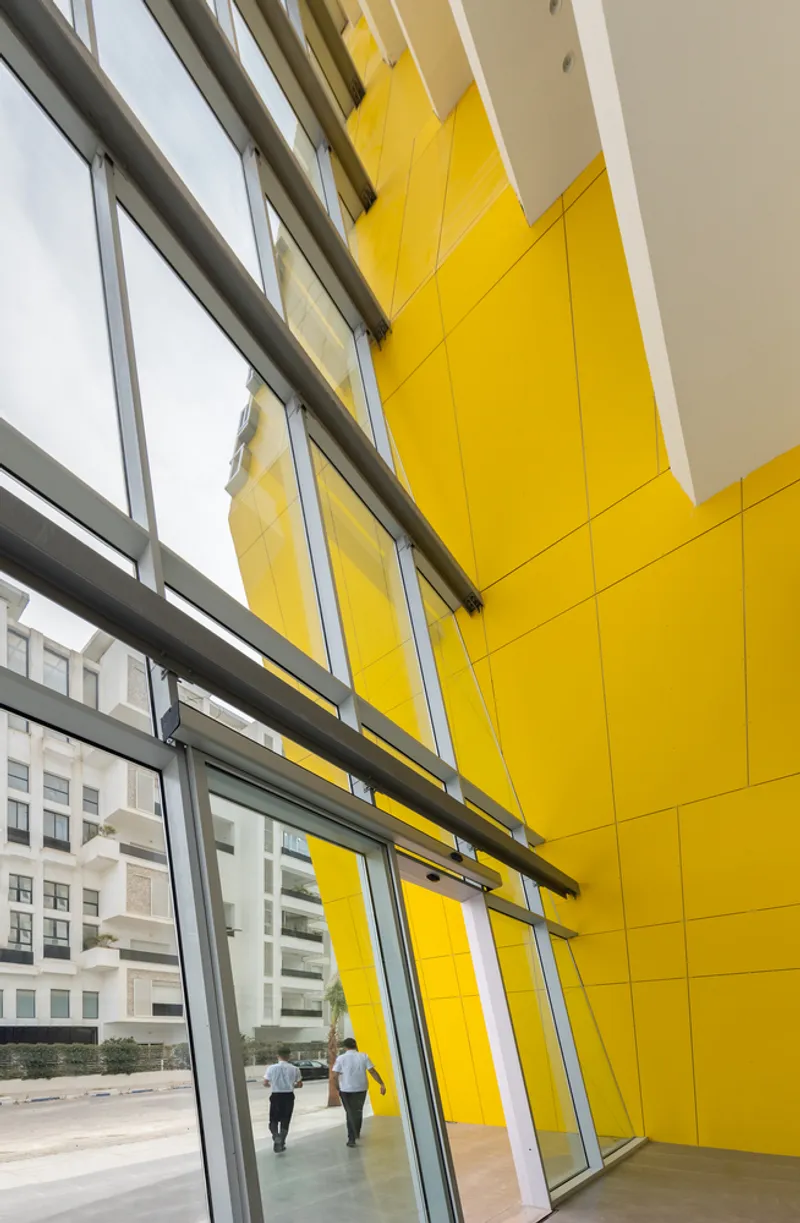 Interior view of yellow soffit and angled glass curtain wall with two people walking through entry lobby