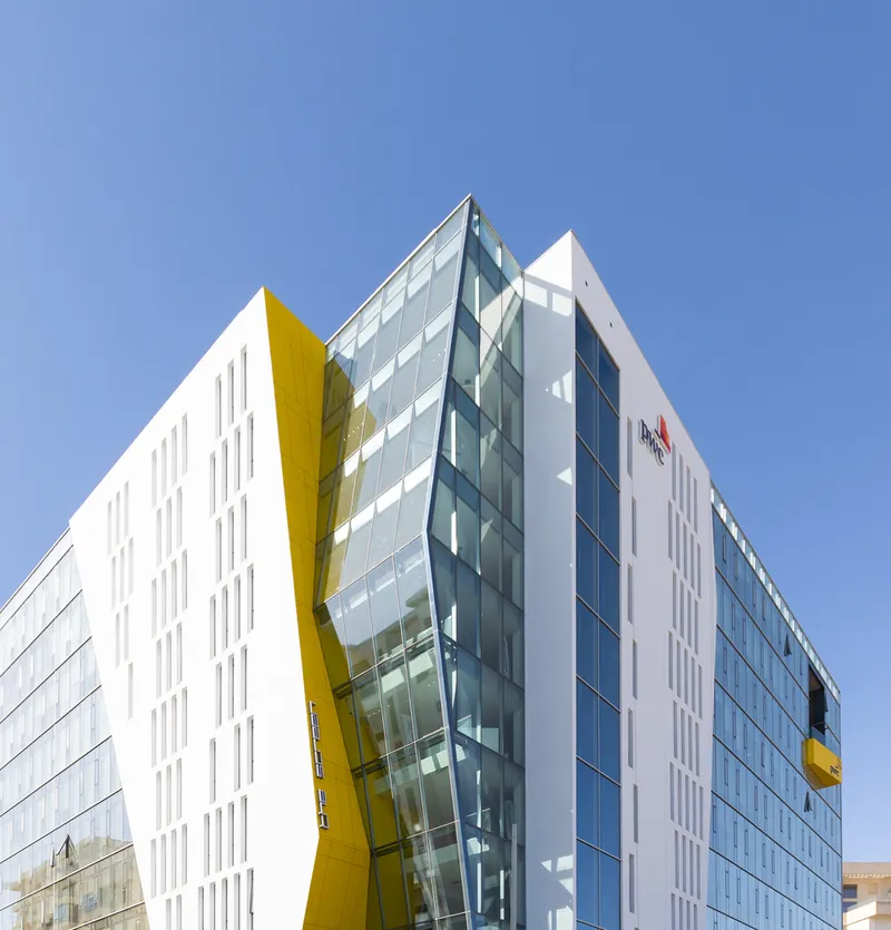 Corner view of the white facade with yellow panel accents and angled glass curtain wall under clear blue sky
