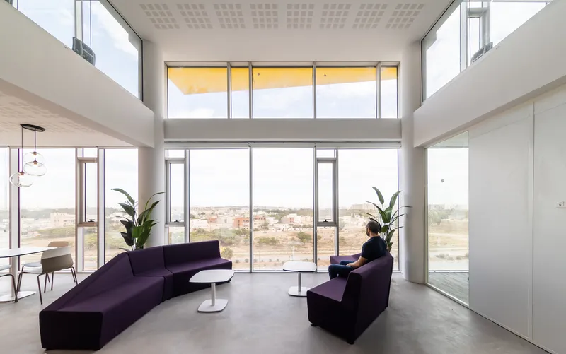Double-height lounge with purple seating, potted plants, and a person seated near the window