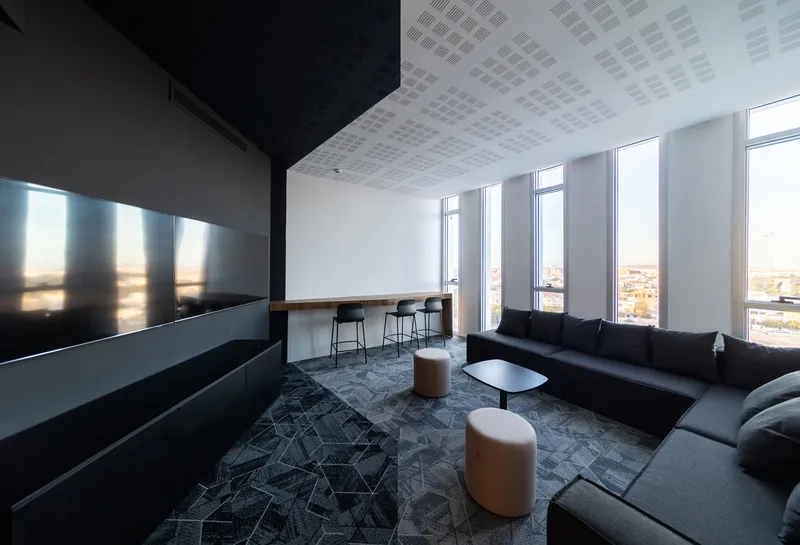 High-floor lounge with perforated acoustic ceiling panels and floor-to-ceiling windows overlooking the city at dusk