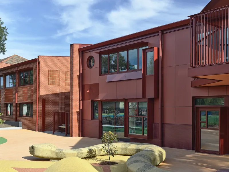 Courtyard view showing red brick and metal panel facades with a sculptural bench and young tree