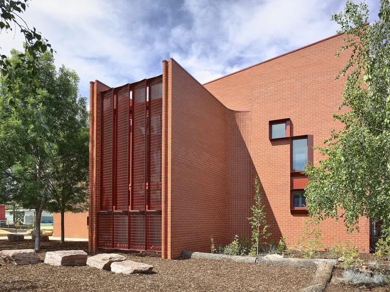 Curved brick wall with angled roofline and vertical metal louver screen flanked by trees