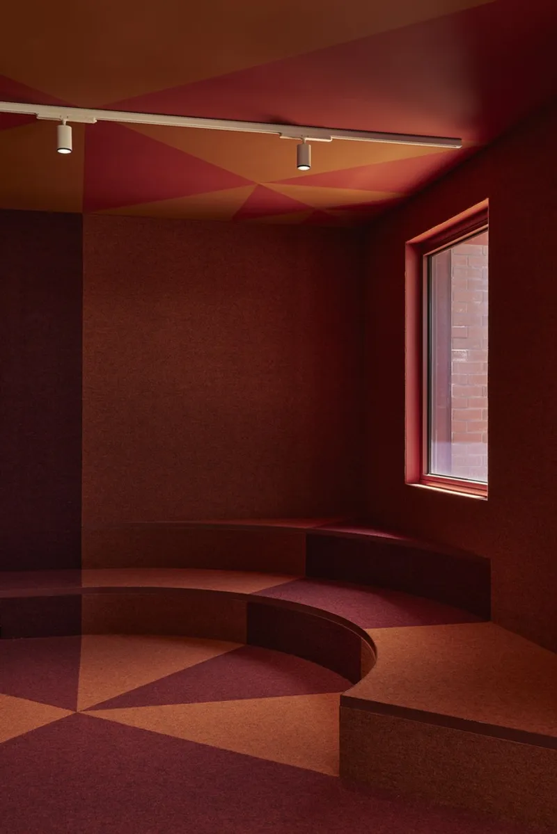 Interior room with curved seating platform in gradient red and orange tones under colored ceiling planes
