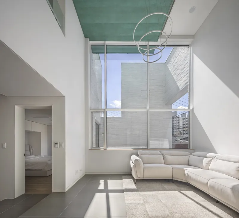Double-height living room with teal ceiling panel and floor-to-ceiling windows casting afternoon shadows