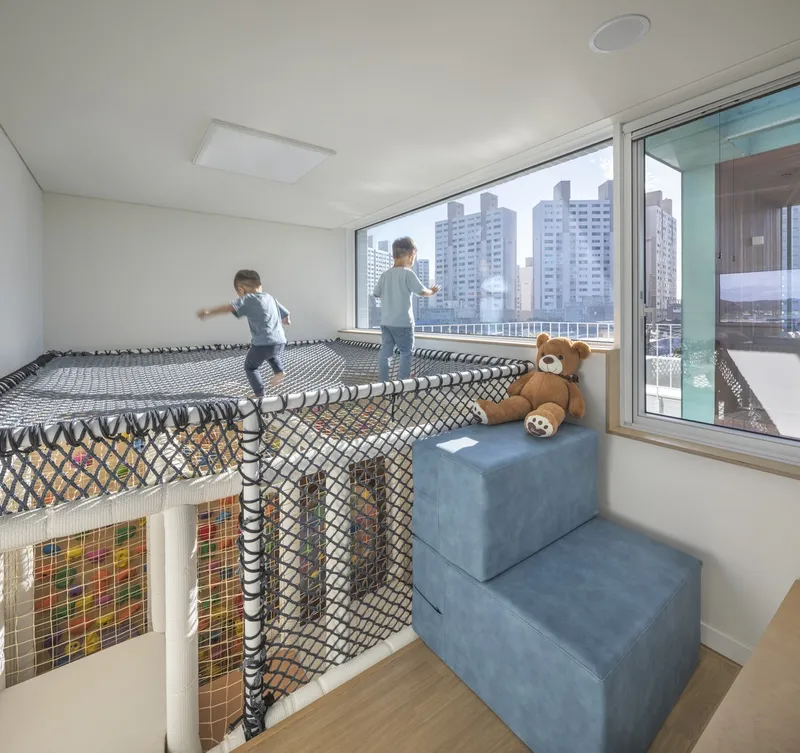 Play loft with rope mesh safety netting and two children visible through glazed balcony doors