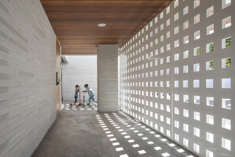 Corridor with perforated concrete block wall creating a grid of light patterns on the floor