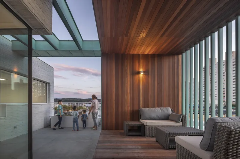 Rooftop terrace with timber-clad ceiling and family gathered at dusk under vertical louver screen