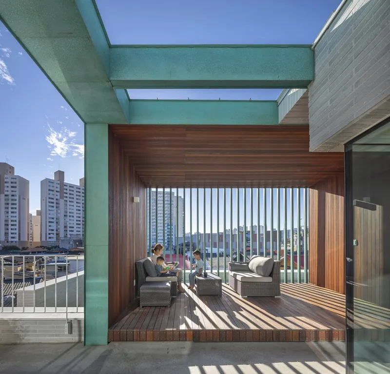 Covered deck pavilion framed by teal beams with vertical timber louvers and two seated figures