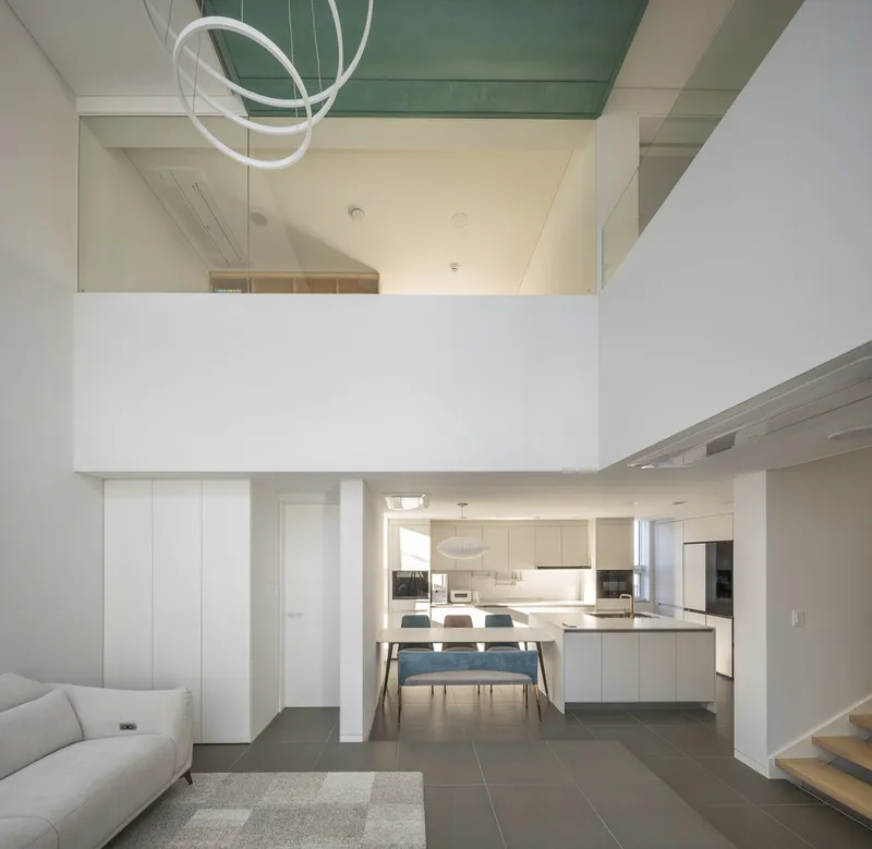 Double-height space overlooking open kitchen and dining area with teal ceiling soffit above mezzanine