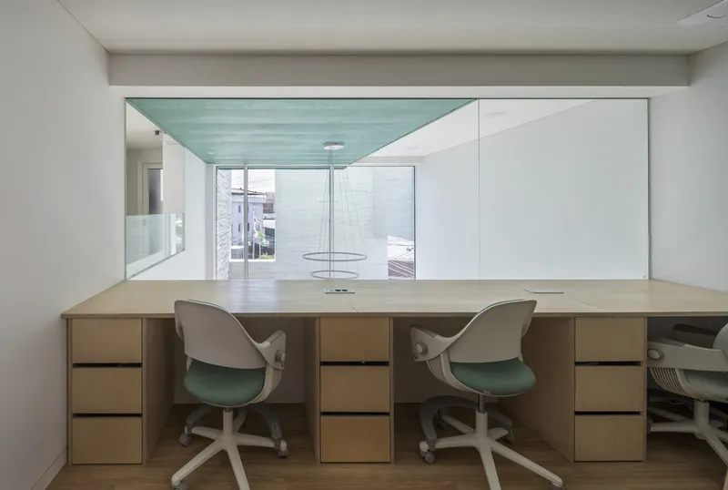 Built-in desk with drawers and chairs facing a glazed opening with a turquoise ceiling panel
