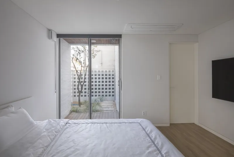 Bedroom with sliding glass doors opening to a small courtyard with a tree and lattice screen