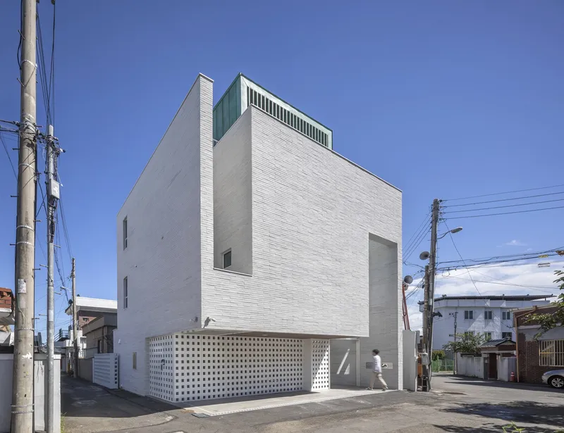 Corner view of the white brick facade with a perforated base and overhead power lines