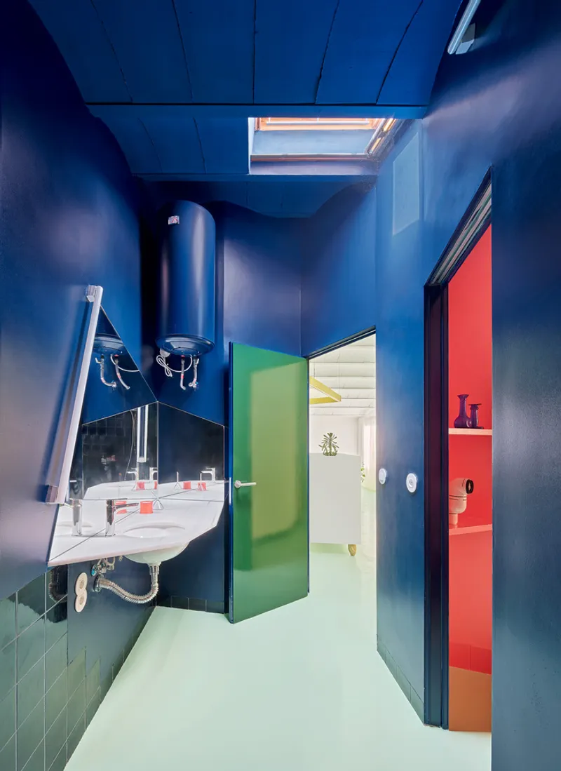 Bathroom corridor with blue walls, skylight above, corner sink, and swinging green and red doors