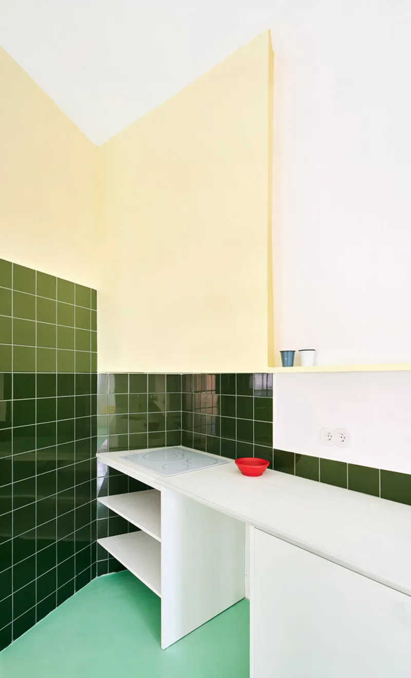 Kitchen corner showing dark green tile walls, white counter with red bowl, and pale green flooring