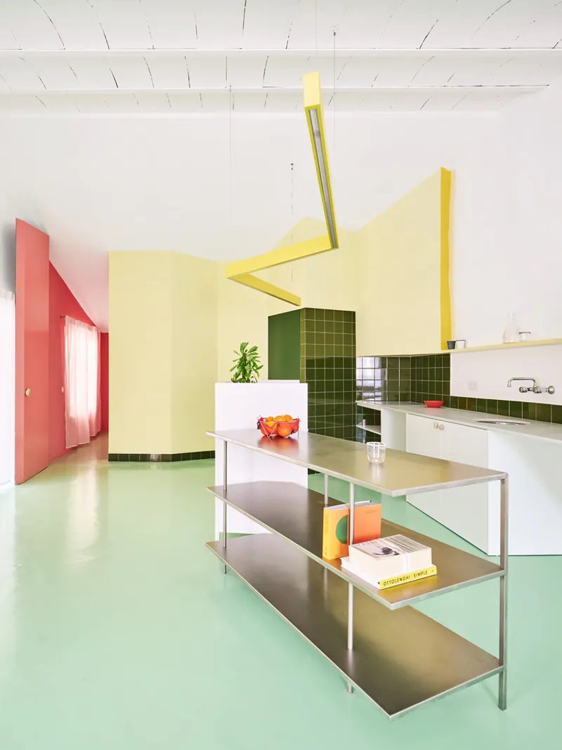 Open kitchen with mint green flooring, steel shelving unit, and yellow angular ceiling elements overhead