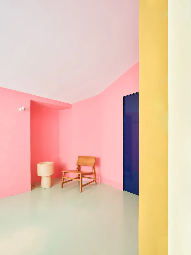 Room with pink gradient walls, pale green floor, wooden chair, and yellow column at the threshold