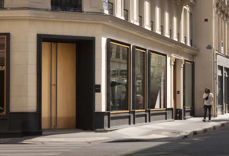 Street facade with black-framed storefront windows and timber double doors set in limestone base