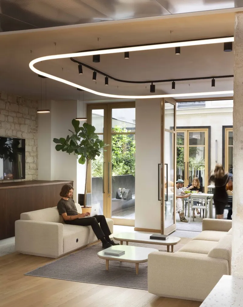 Lounge space with curved illuminated ceiling fixture and glass doors opening to green courtyard