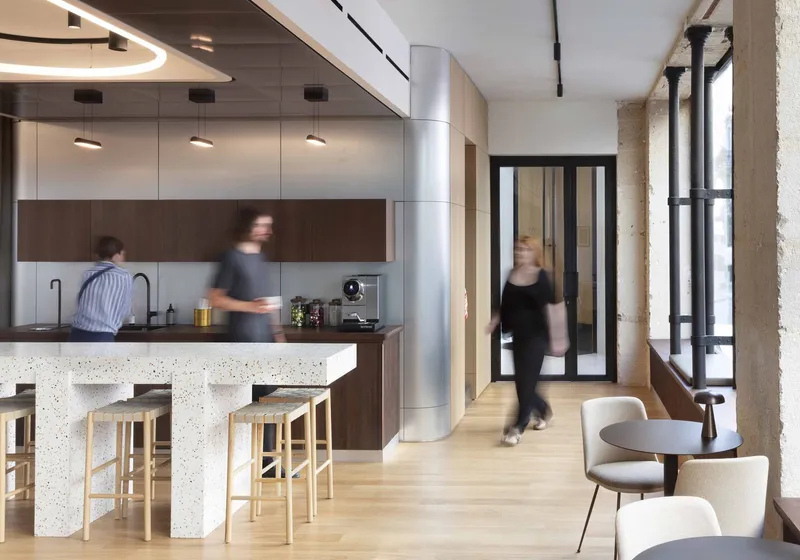 Open kitchen and lounge area with terrazzo island and blurred figures passing through