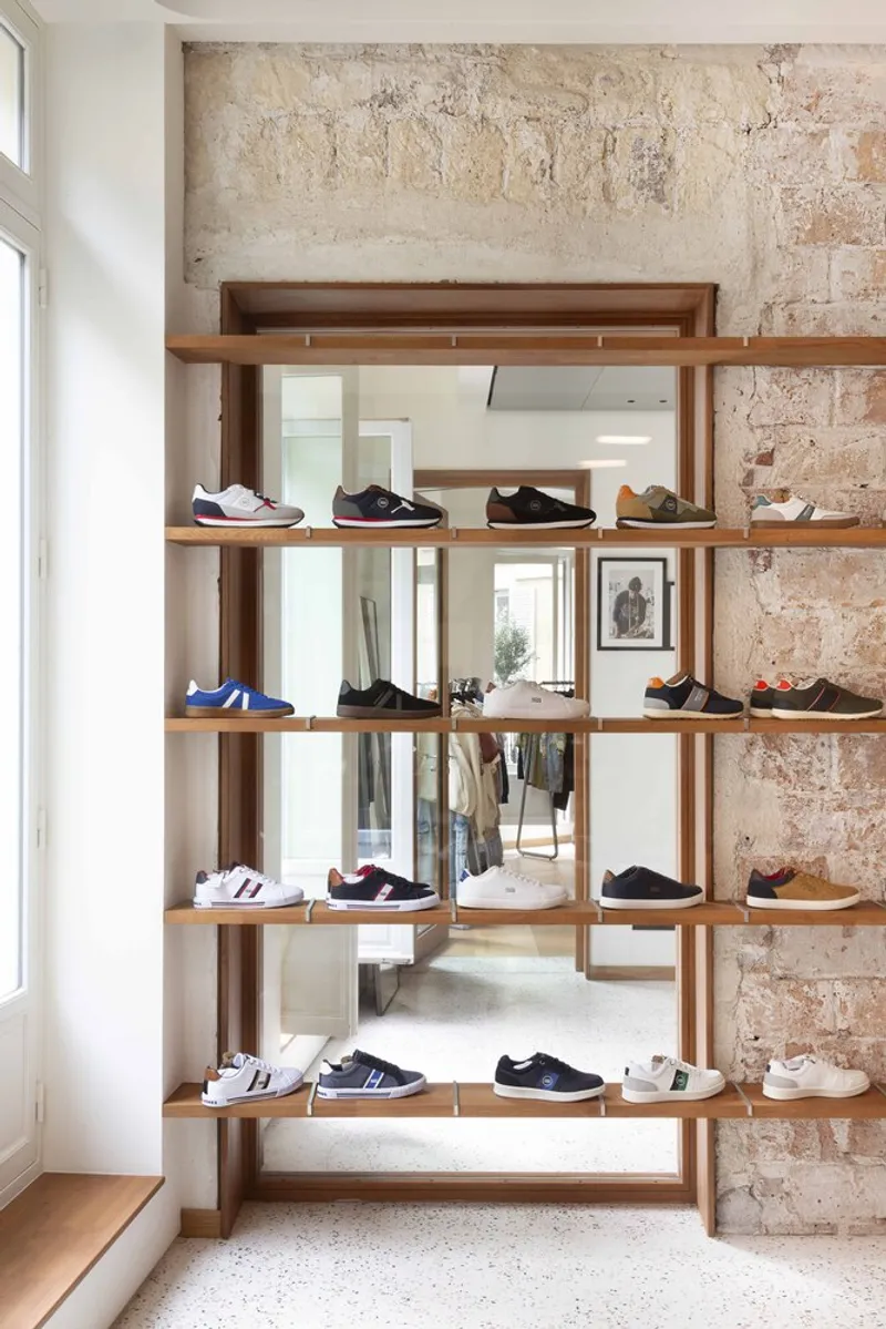 Timber shelving unit displaying sneakers against exposed masonry wall with daylight from side window