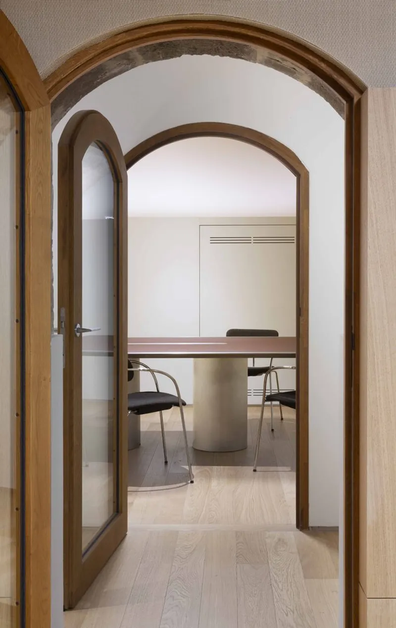 View through arched timber doorway into a meeting room with cylindrical concrete base table