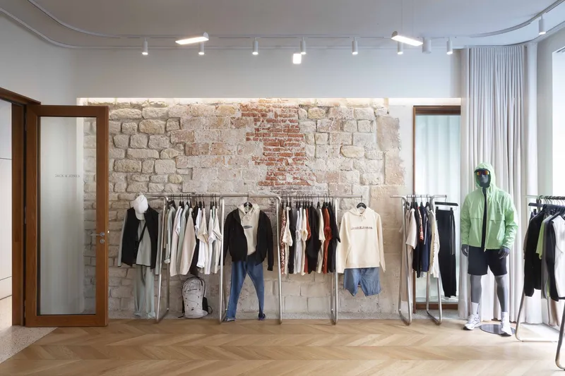 Retail interior with exposed stone and brick wall behind clothing racks and herringbone oak flooring
