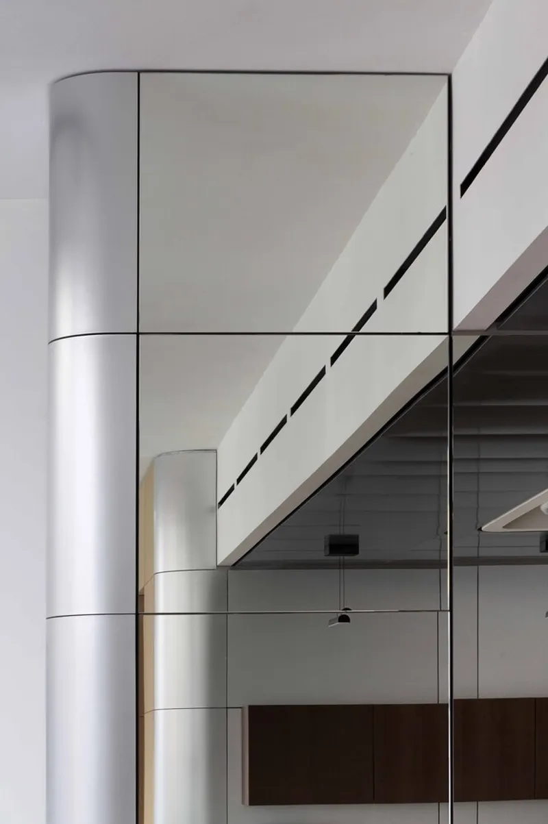 Interior view of cylindrical white column beside glass-railed staircase under linear skylight