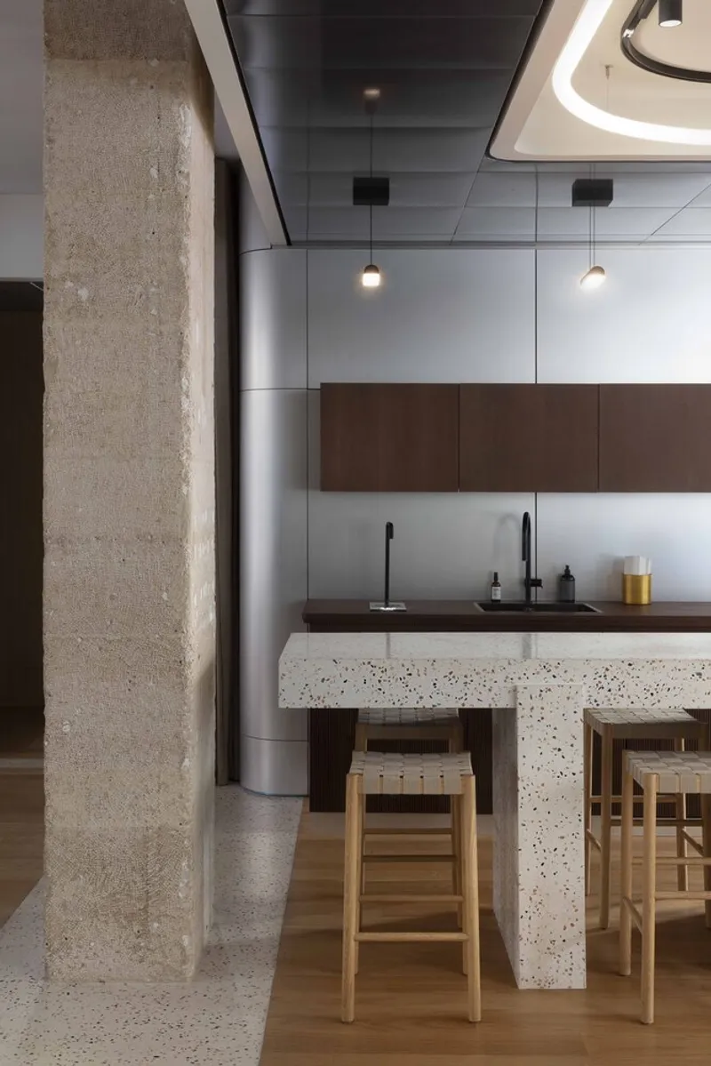 Kitchen counter with fluted walnut base, terrazzo waterfall edge, pendant lights and exposed stone column