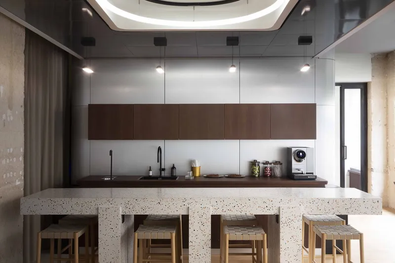 Terrazzo island with timber stools beneath a rounded skylight and suspended lighting fixture