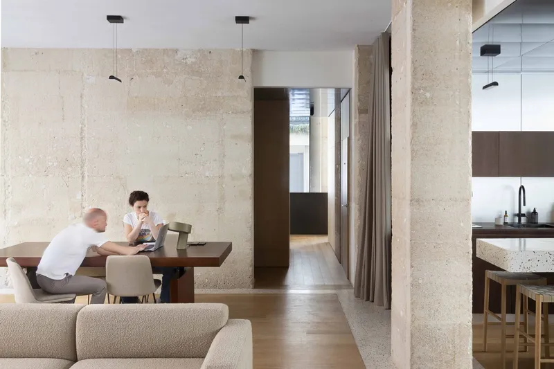 View through exposed concrete columns toward a corridor with occupants at a timber table
