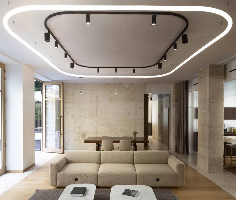 Living area with beige sofa facing a dining table beneath a rounded recessed ceiling fixture