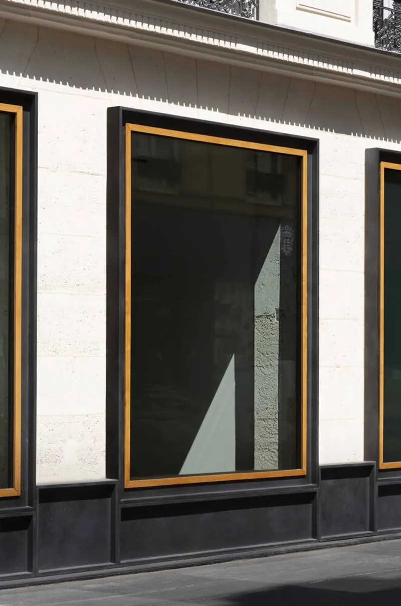 Street facade detail showing gold-framed window with black surround and dark base panel in pale masonry