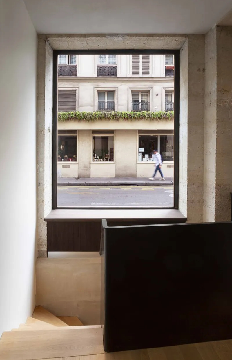 Deep window recess framing view of street with pedestrian crossing past shopfront below planted balcony
