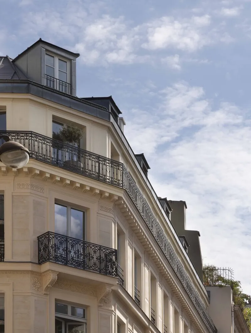 Corner facade with wrought-iron balconies and mansard dormers beneath scattered clouds