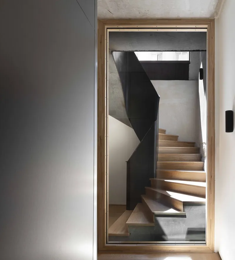 View through timber-framed doorway to timber staircase with black steel balustrade and skylight above