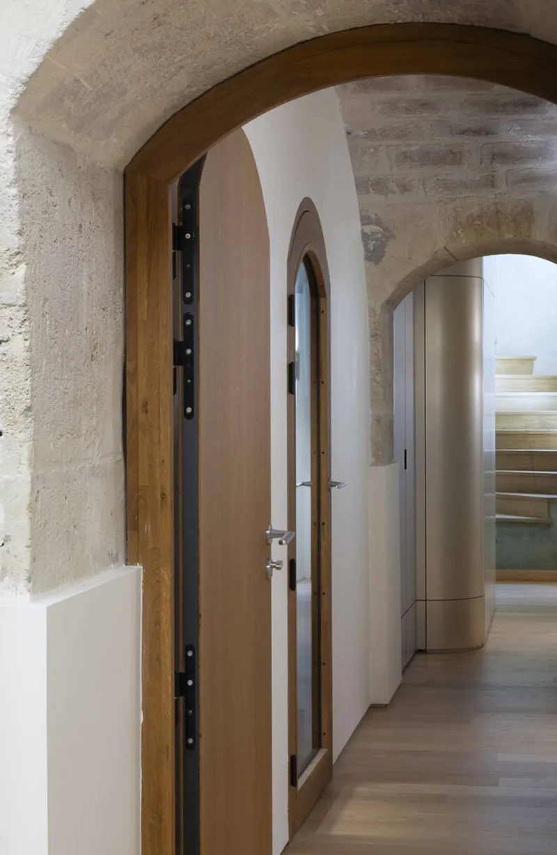 Arched stone corridor with timber-framed doors and glimpse of curved metallic volume beyond