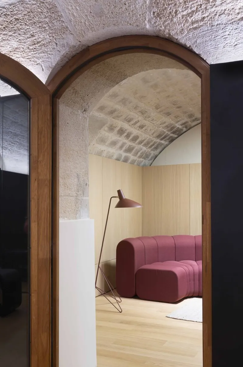 Timber-framed arched opening revealing barrel-vaulted stone ceiling above pink sofa and standing lamp