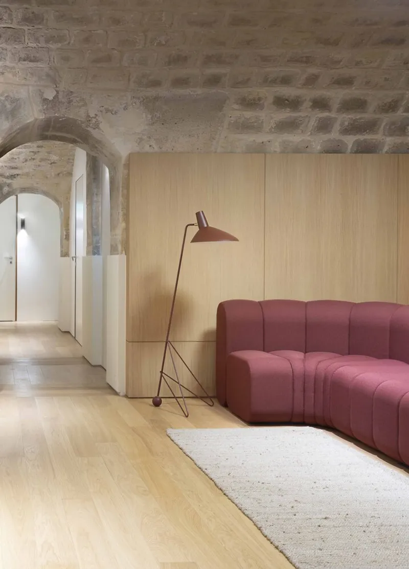 Light wood paneled wall with pink upholstered sofa and floor lamp beneath arched stone ceiling