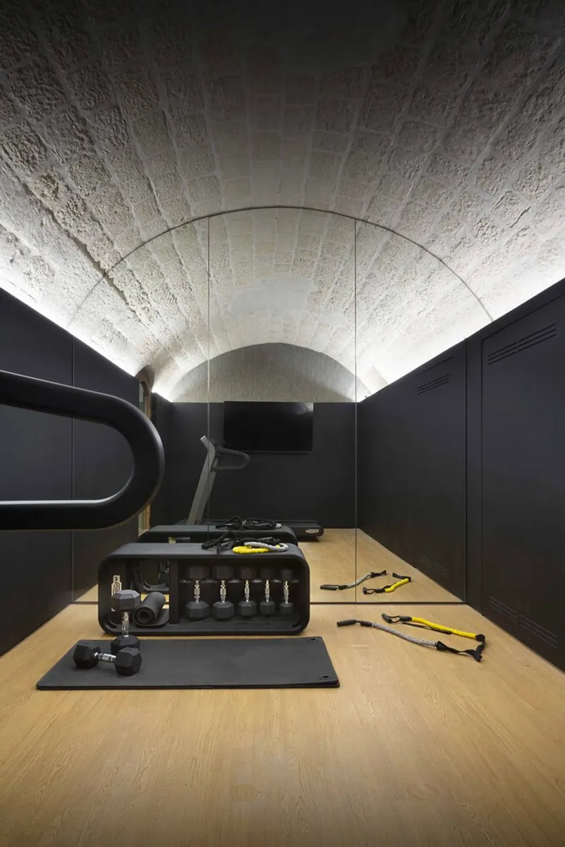Fitness room with exercise equipment under barrel-vaulted stone ceiling flanked by black cabinetry