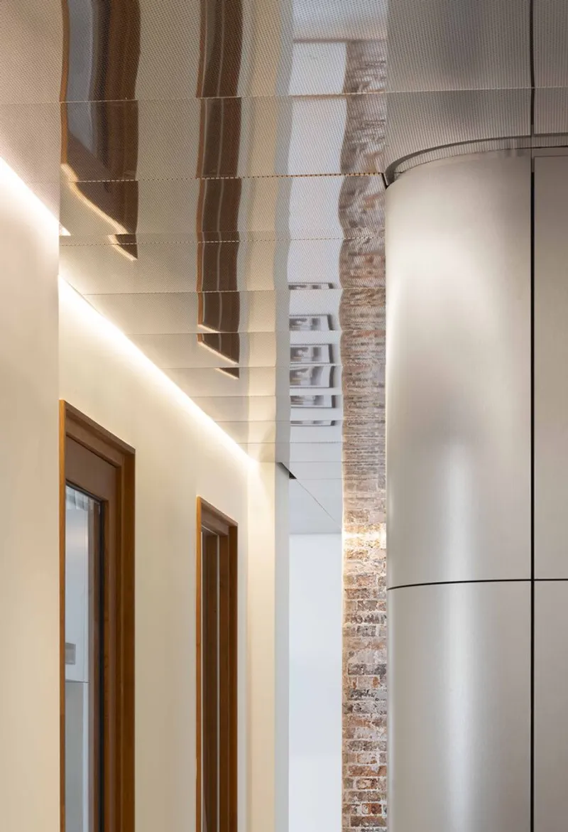 Double-height interior showing timber doors and exposed brick wall alongside reflective metal ceiling panels