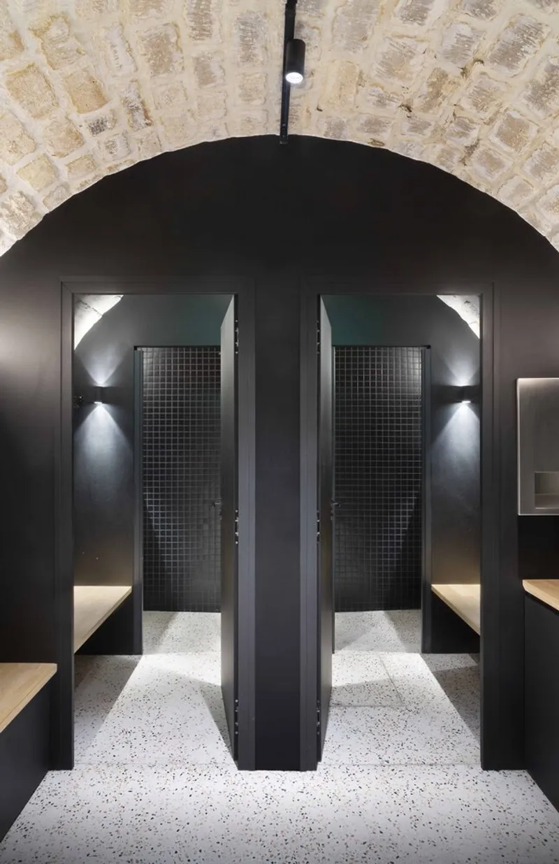 Black-painted arched passage framing two shower enclosures with mesh glass doors and wall sconces