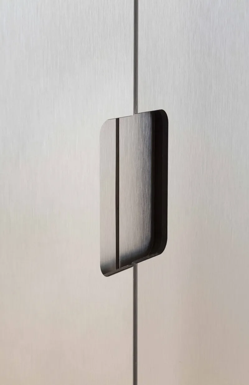 Detail of rounded metal door pull mounted on brushed aluminum panel joint