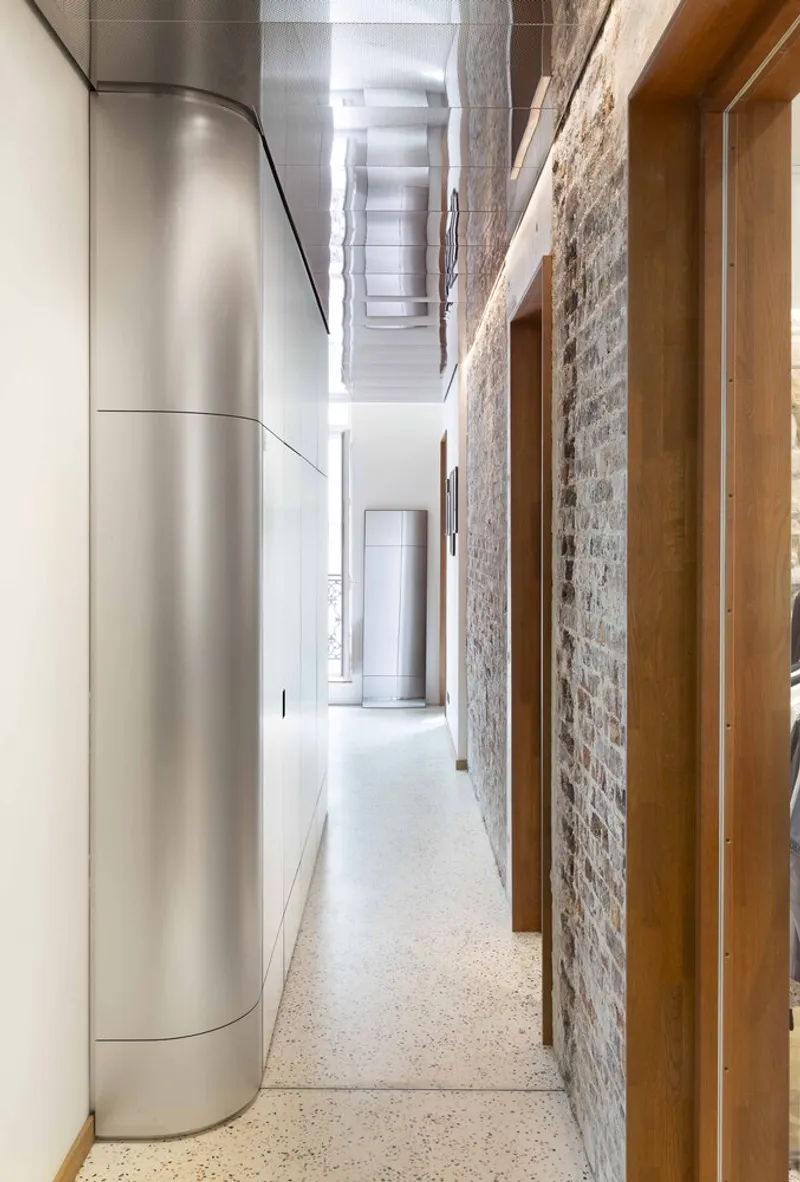 Long hallway with curved brushed metal wall opposite weathered brick and timber door frames