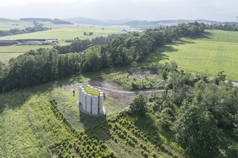 Aerial: sandstone chapel on a hillside above rolling green farmland and trees in Germany