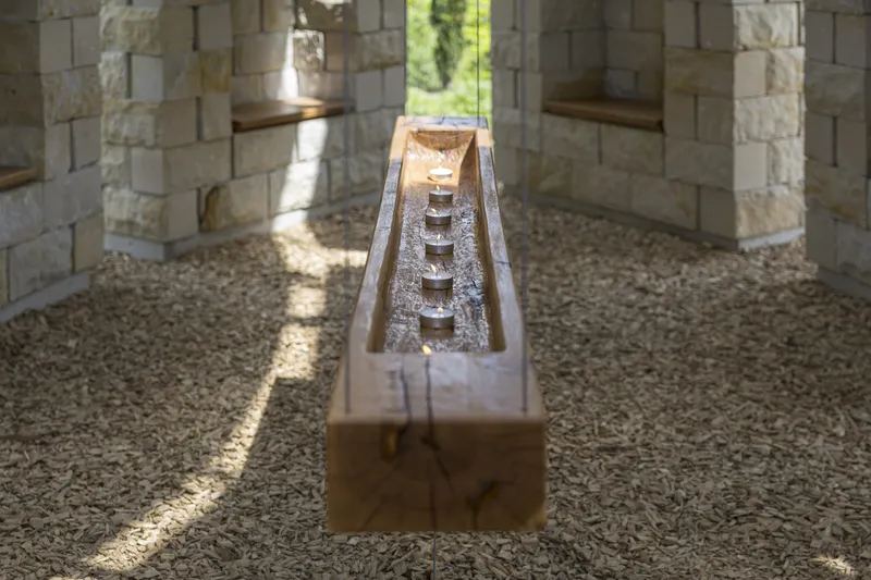 Detail: timber trough with row of votive tealight candles, gravel floor, sandstone walls