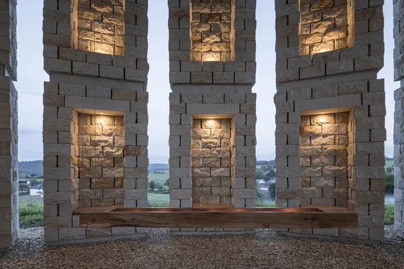 Three niches with lit interior glow framing the view to landscape, timber bench at the bottom