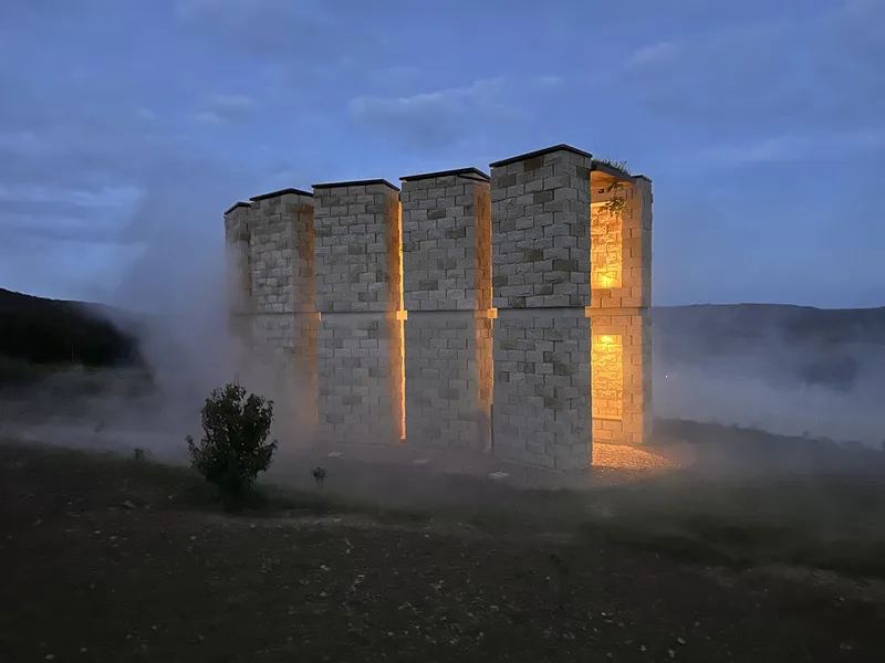 Night exterior: chapel as a glowing ring of stone columns in the mist, vegetation in the foreground