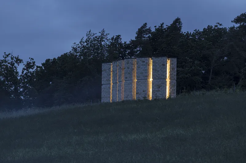 Dusk from the meadow: stone columns with warm light glowing through the gaps, grass in the foreground