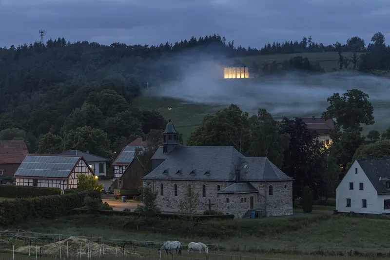 Night view from the village: chapel on the hilltop above the existing church, fog in the valley