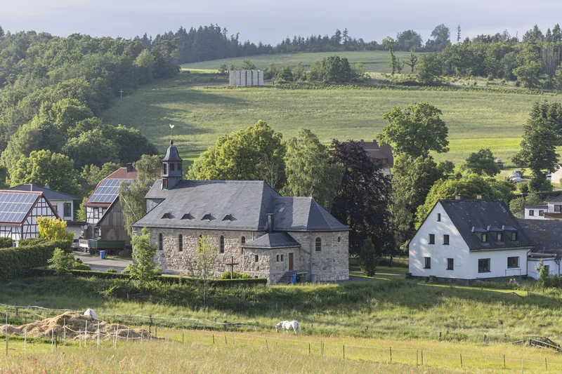 View of the village and farmland with the existing stone church at centre, new chapel visible on the hilltop in the distance